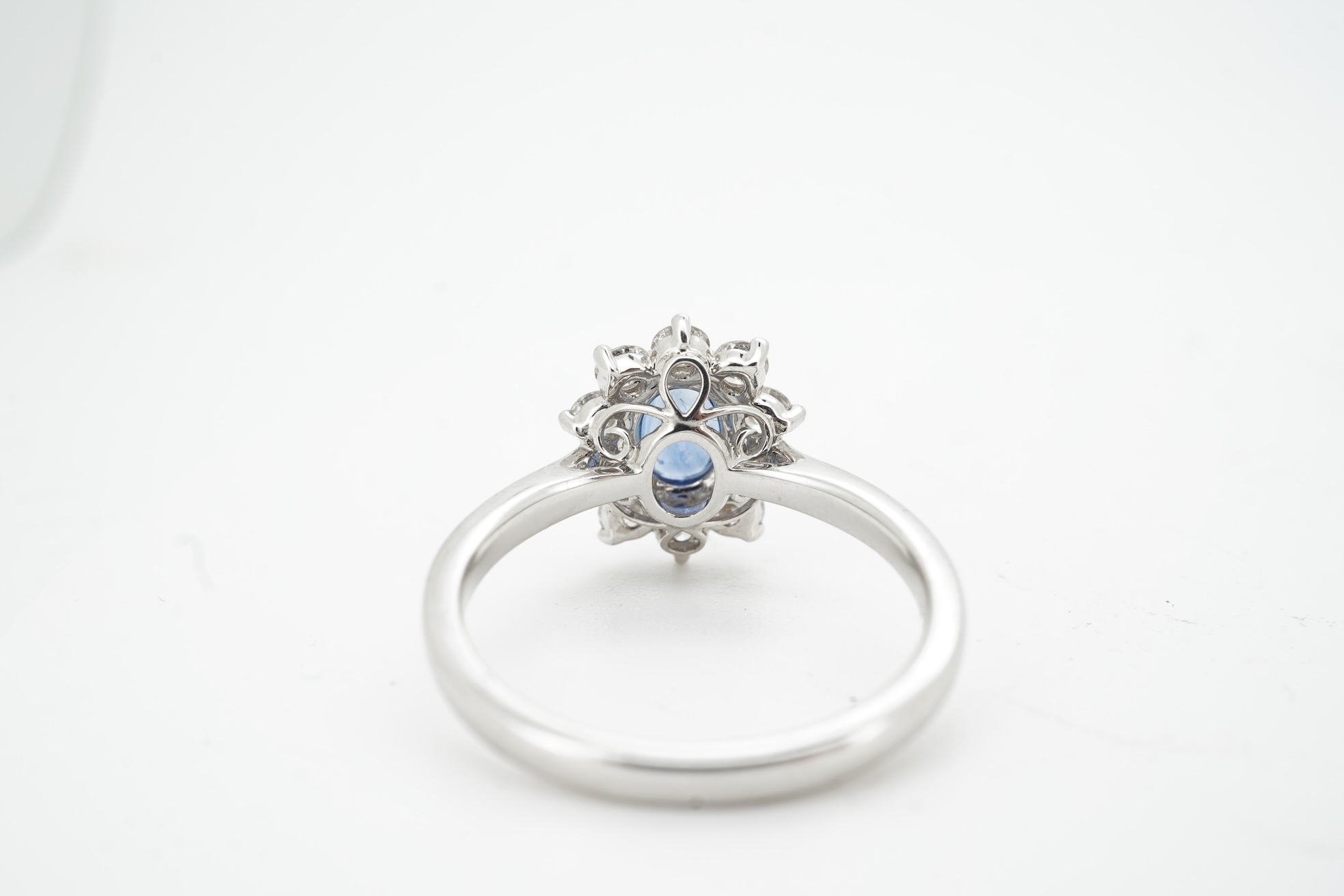 A sapphire and diamond cluster ring, claw-set with an oval sapphire weighing approximately 0.77 carats, within a border of brilliant-cut diamonds totalling approximately 0.50 carats, mounted in white gold, size M, stampe